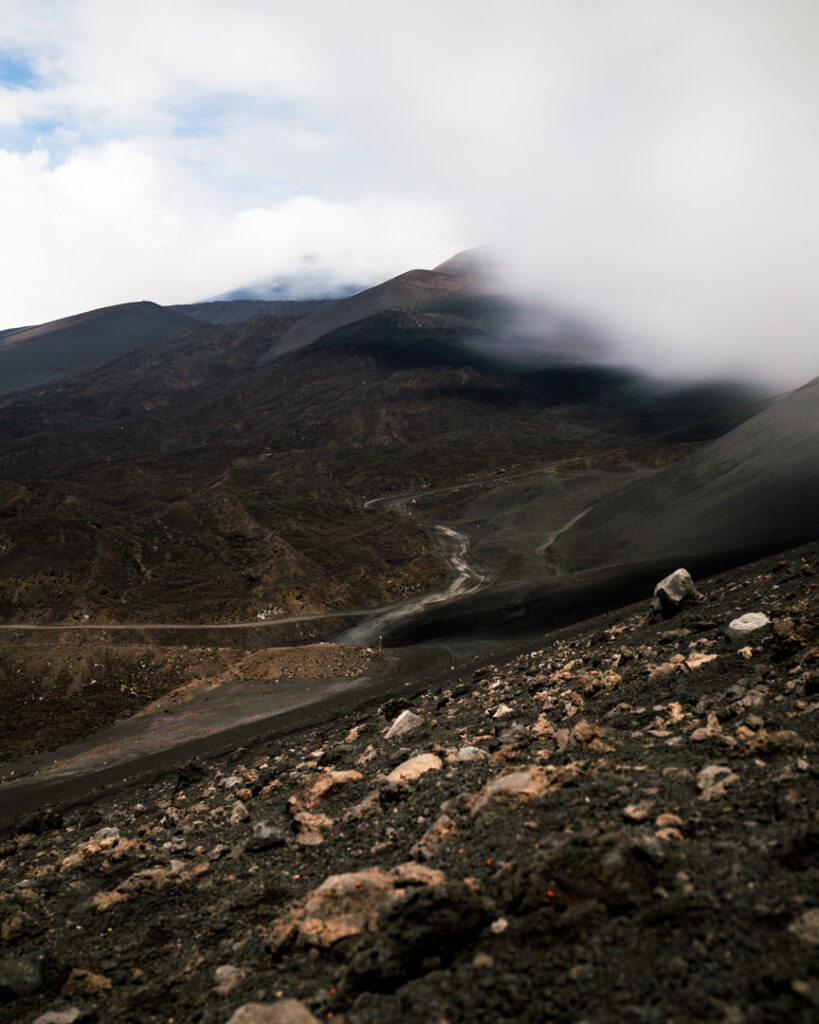 Aufnahme an einem der Krater des Ätnas. Der Weg hinauf zum Hauptkrater. Schwarzes Lavagestein mit Marienkäfern im Vordergrund.